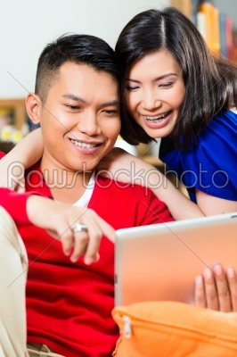 Young Indonesian couple - man and woman - sitting with a tablet computer on a couch