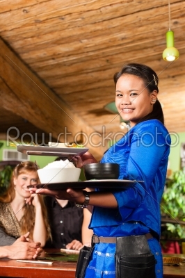 Young people with waitress eating in Thai restaurant