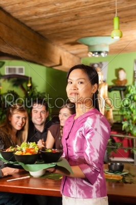 Young people with waitress eating in Thai restaurant