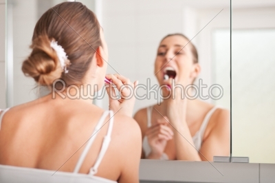 Young woman brushing teeth at wash bowl 