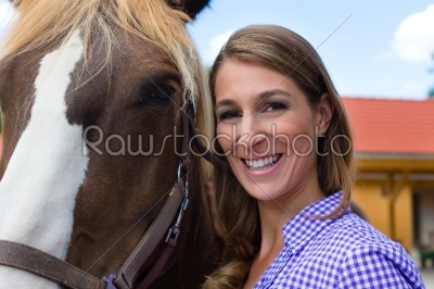 Young woman in the stable with horse in sunshine