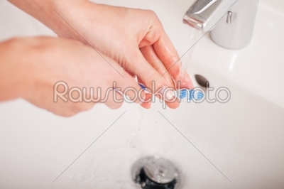 Young woman (just hands) cleaning her teeth brush 