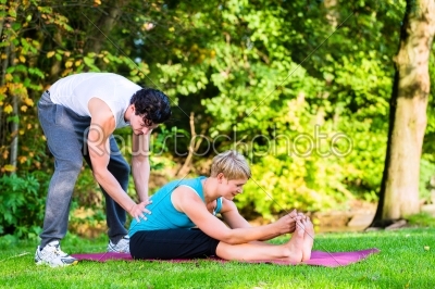 Young woman outdoors doing yoga with trainer