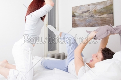 angry couple fighting together with pillows in bed having confli