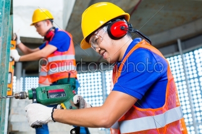 Asian construction workers drilling in building walls