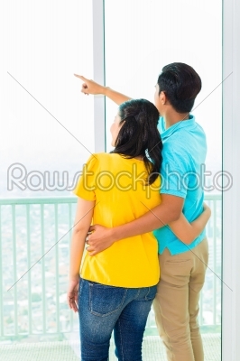 Asian couple looking out of apartment window 