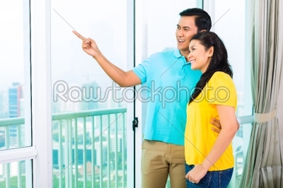 Asian couple looking out of apartment window 