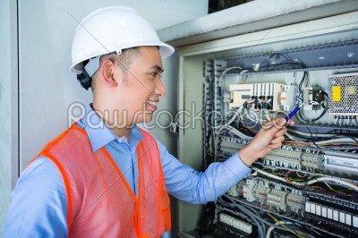 Asian Electrician at panel on construction site