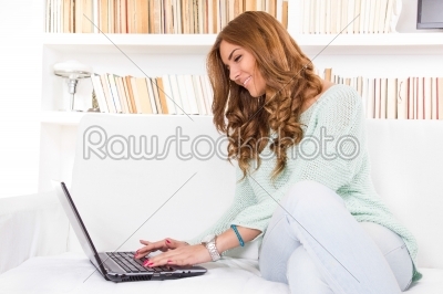 attractive smiling woman using laptop computer keyboard on sofa