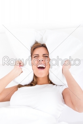 Beautiful woman is lying in bed and covering her ears with pillo