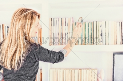 beautiful young woman taking a book from shelf in library