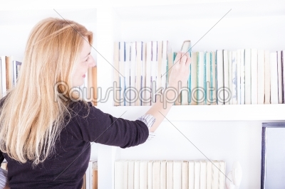 blond woman pulling a library book off shelf
