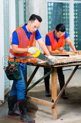 Builder sawing a wood board of building or construction site 