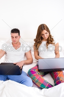 casual bed couple on two laptop computers in bedroom