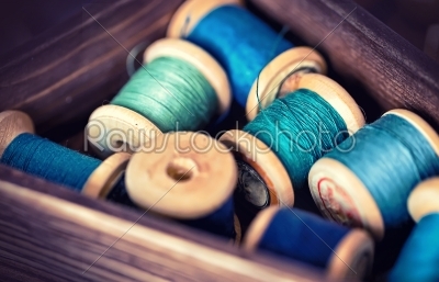 Collection of aqua spools threads arranged in a grunge wooden box