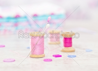 Collection of spools  threads in pink colors arranged on a white wooden background