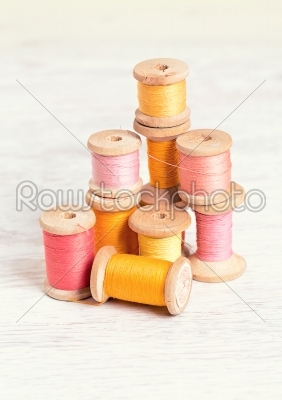 Collection of spools  threads in yellow-red colors arranged on a white wooden background