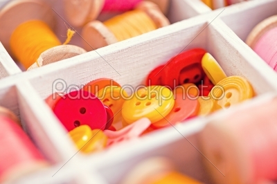 Collection of yellow, red, pink  buttons  arranged in a white wooden box