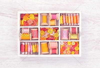Collection of yellow, red, pink spools  threads  arranged in a white wooden box