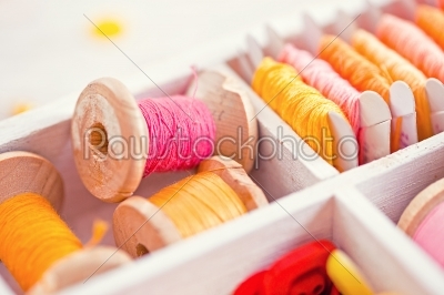 Collection of yellow, red, pink spools  threads  arranged in a white wooden box