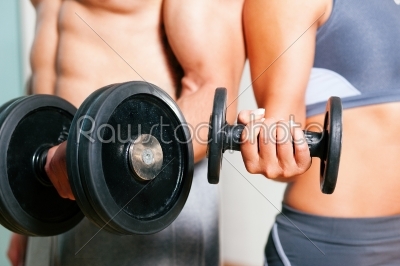 Couple exercising with dumbbells in a gym, focus on the weights, only torso of man and woman to be seen