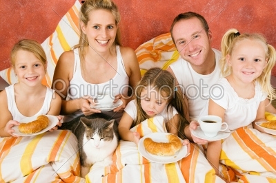 Family and cat having breakfast in bed