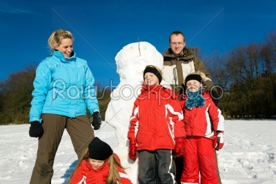 Family in winter standing in front of their snowman