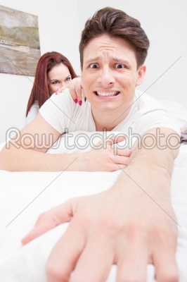 frightened man trying to escape from the bed because woman
