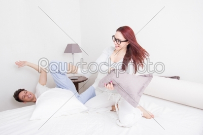 girl in pajamas hitting her boyfriend with pillow while he falli