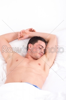 half naked man with both hands up on pillow sleeping in bed