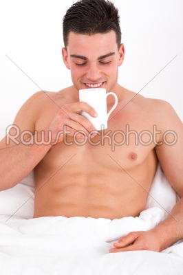 handsome man in bed enjoys the smell of coffee
