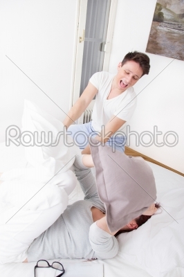 happy boy in pajamas hitting girl with pillow