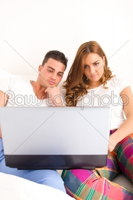 happy couple enjoying using laptop computer in bed