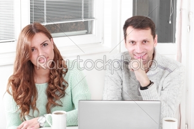 Happy couple looking at camera with laptop at home