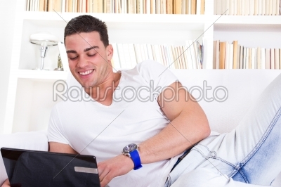 happy young man lying on sofa working on laptop computer