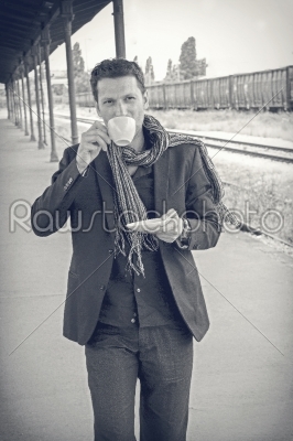 male model drinking coffee at train station