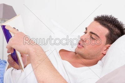 man lying in bed reading book