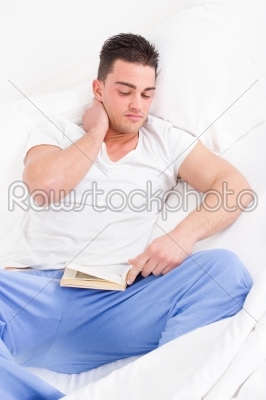 man lying in bed suffering from neck pain reading book