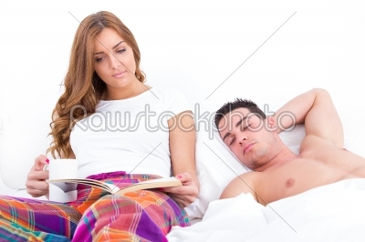 man sleeping while his girlfriend is reading in bed