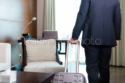 Manager in suit moving into hotel room with his suitcase
