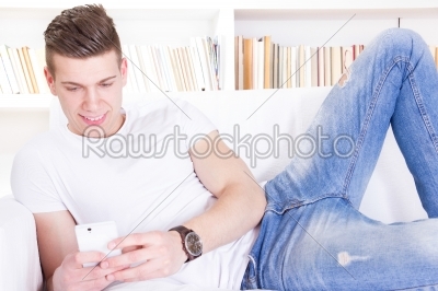 modern guy using smart phone relaxing on sofa at home