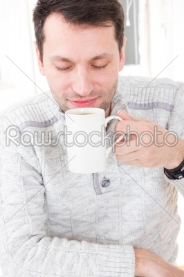 Morning portrait of handsome guy smelling and holding coffee cup