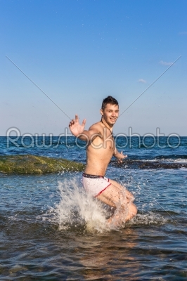 Naked young man jumping for joy from see water