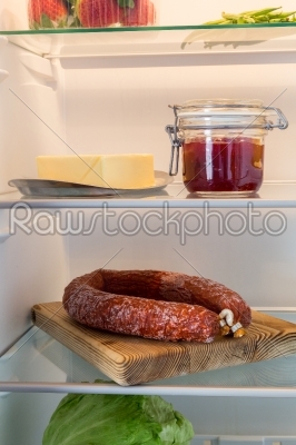 Open fridge stuffed with salami and foodstuffs