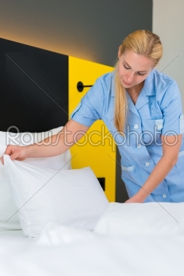 Service in hotel, maid puts clean sheets on bed