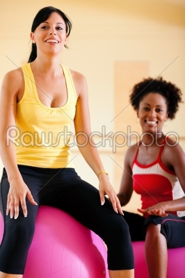 Two women with fitness ball in gym
