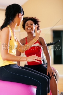 Two women with fitness ball in gym