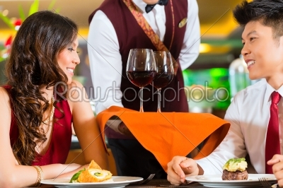 Waiter serving Chinese couple wine in fancy restaurant