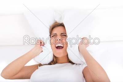 Woman screaming and covering her ears with pillow because of noi
