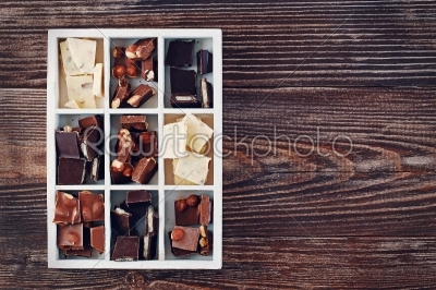 Wooden box with set of dark, white and milk chocolate on wooden table